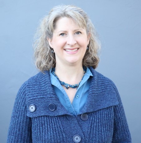 Michelle Bronson in blue button up sweater, blue necklace and blue backdrop