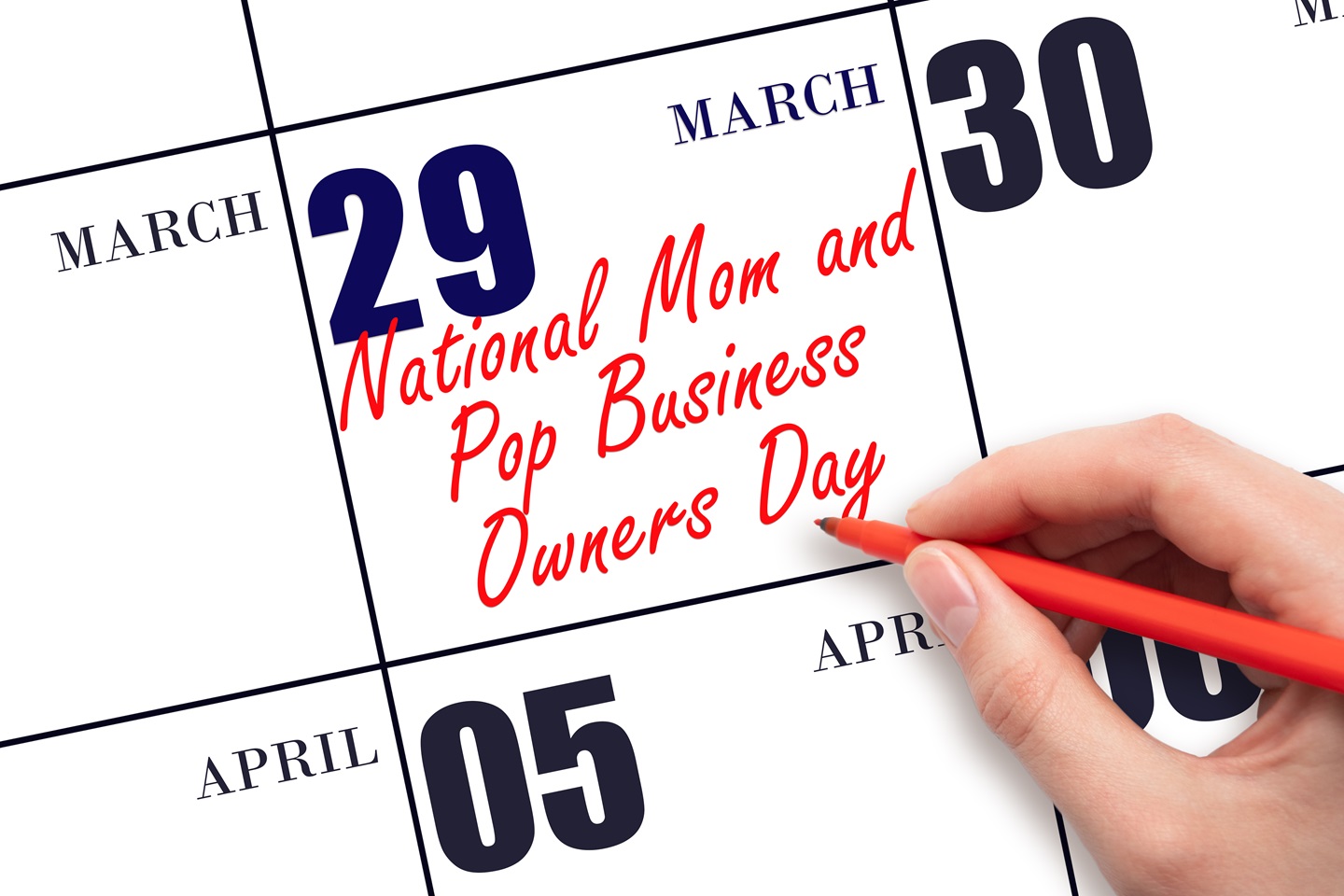 A zoomed up picture of a person writing on a calendar under the number 29 "National Mom and Pop Business Owner Day."