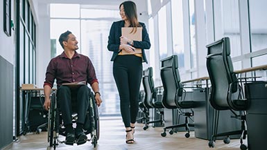 Male coworker in wheelchair having a cheerful conversation with female coworker in office hallway.