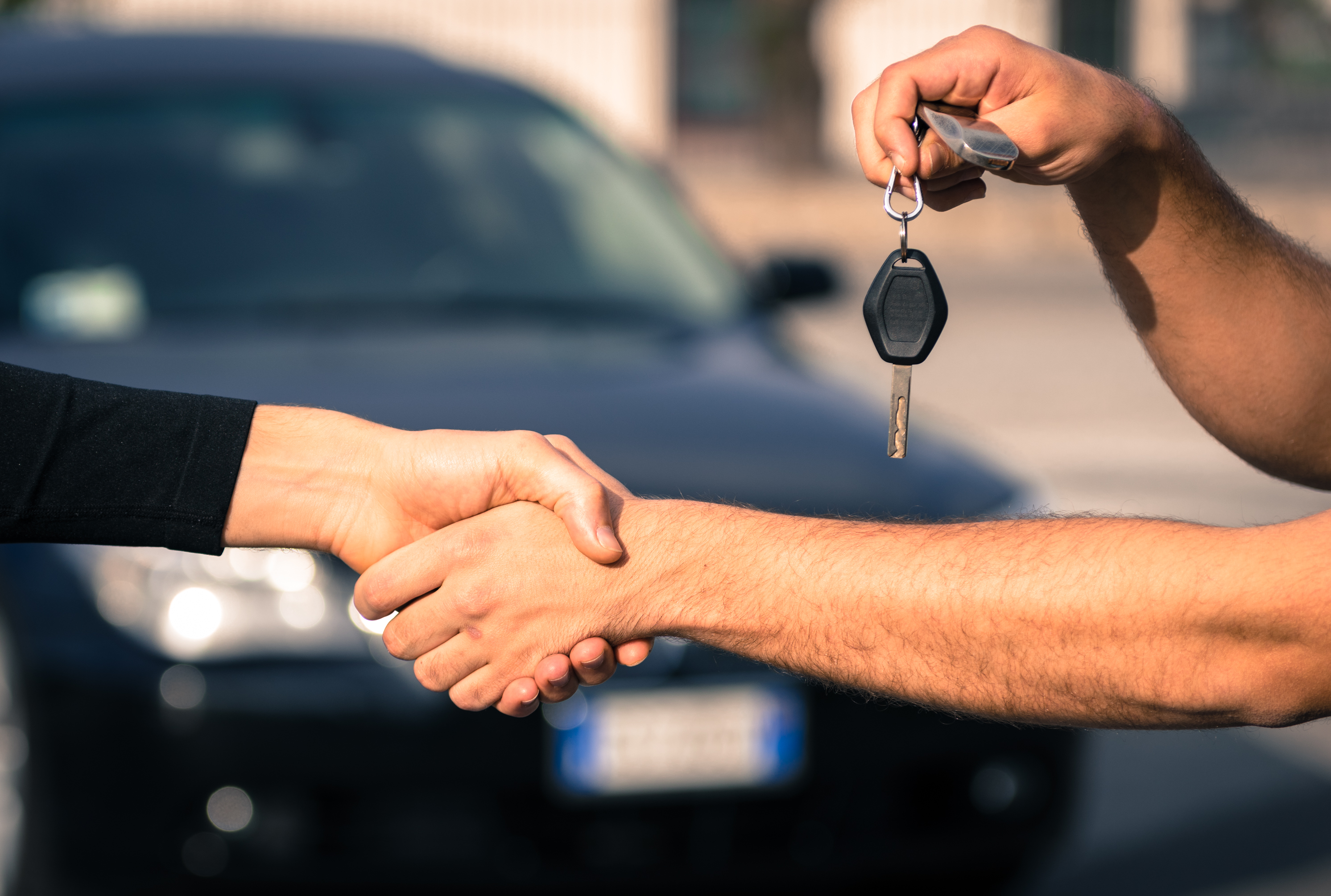 Picture of two people shaking hands. One person is holding a car key.
