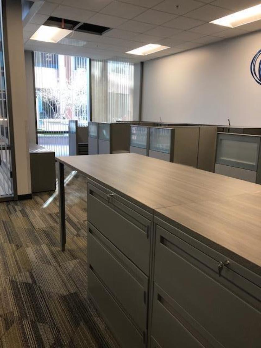 View of collaborative workspace with storage  unit that doubles as a standing work surface and three cubicles to the right. 