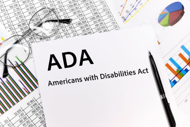 A pile of papers with a pair of reading glasses and a pen. The top paper reads, "ADA - Americans with Disabilities Act", below that paper is several financial documents.